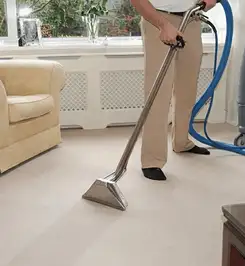 Professional carpet cleaner using a hot-water extraction wand and hose machine in a living room in Kansas City, KS.