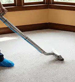 Steam carpet cleaning technician using a hot-water extraction wand on a residential carpet, wearing blue protective shoe covers Kansas City, KS.