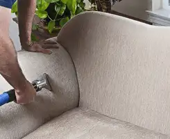 Professional upholstery cleaner deep-cleaning a fabric sofa with a handheld extraction tool and hose in Kansas City, KS.